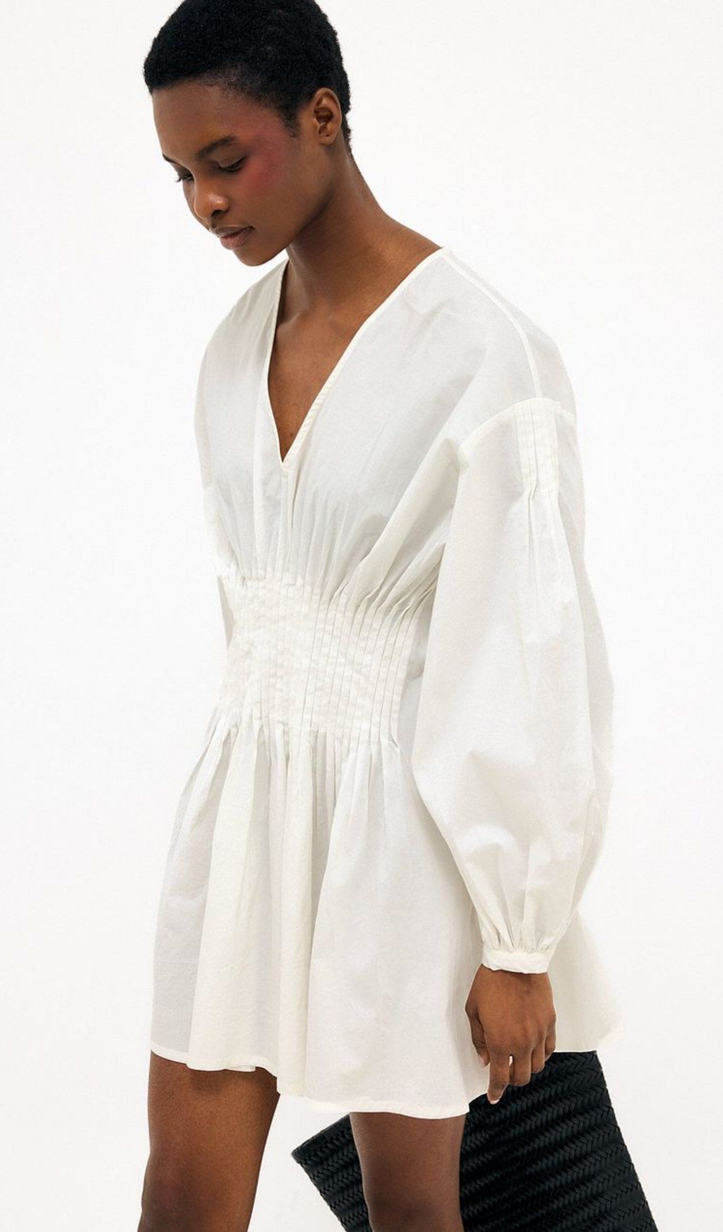Model wearing a white mini dress with long puff sleeves and smocked waist, standing in front of white background