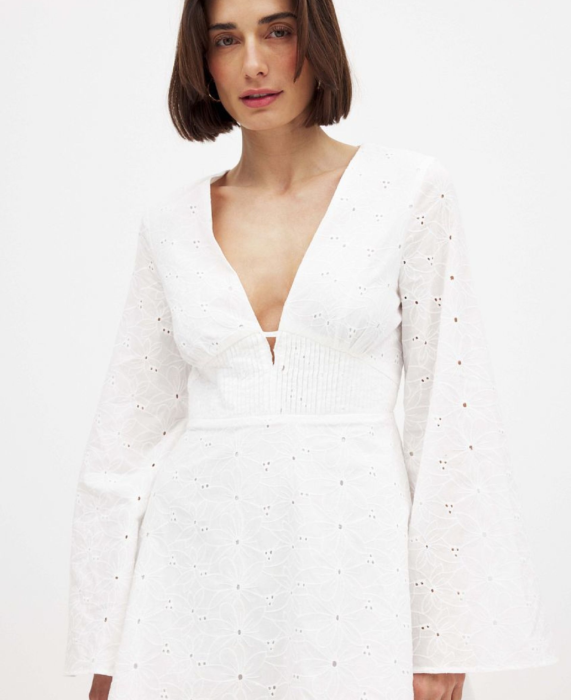 White long sleeve mini dress with deep V neckline and subtle eyelet detailing modeled against a clean studio background