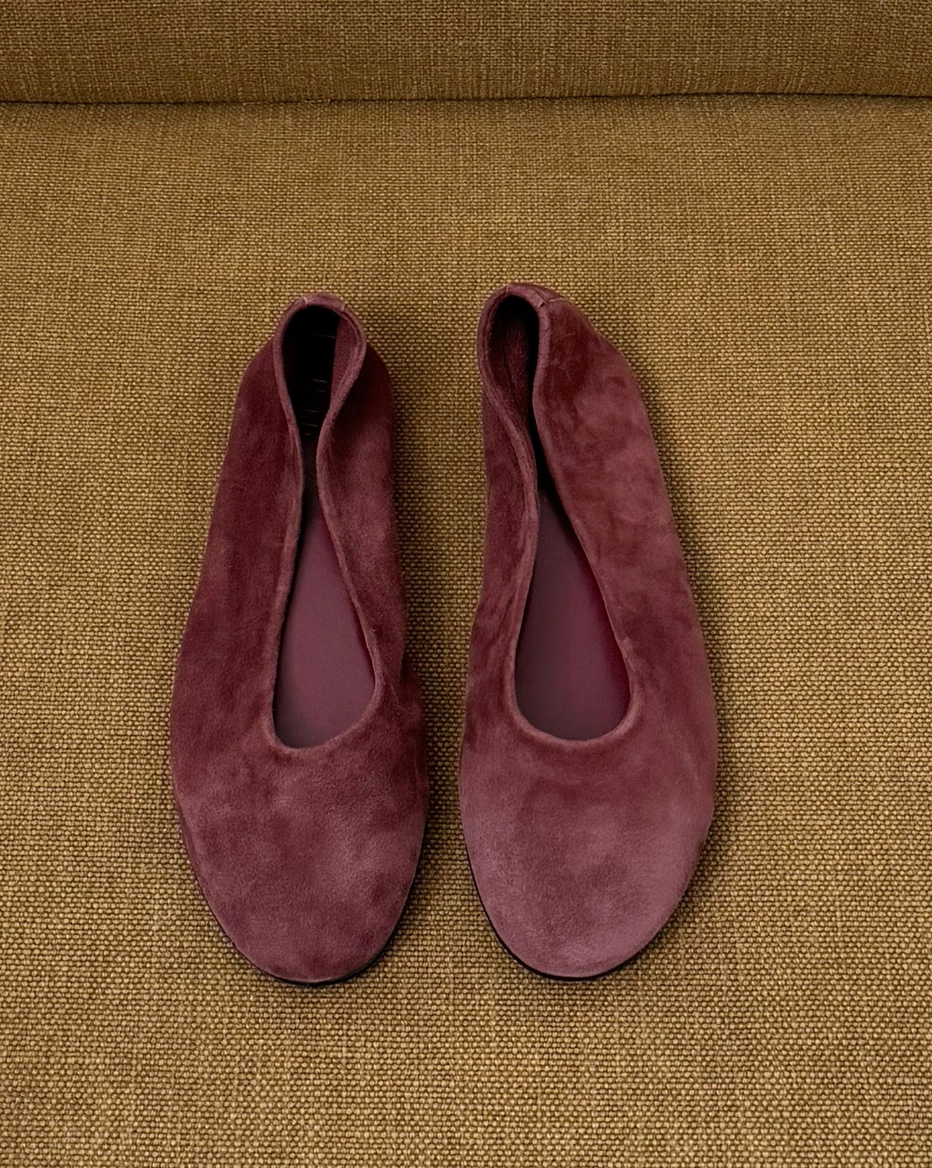 Burgundy suede ballet flats placed on mustard upholstered chair seat