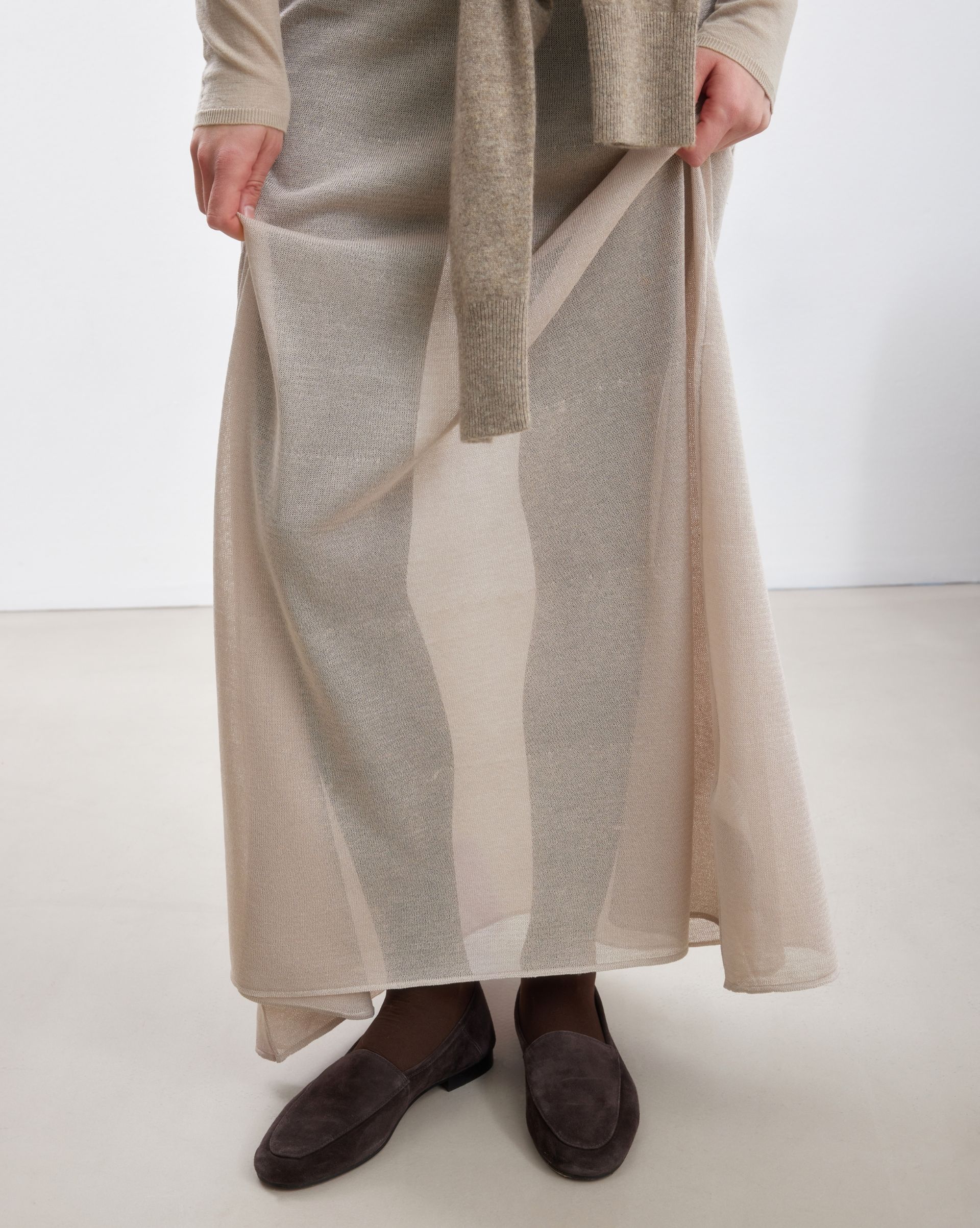 Close-up of beige sheer knit skirt layered over leggings with brown suede loafers