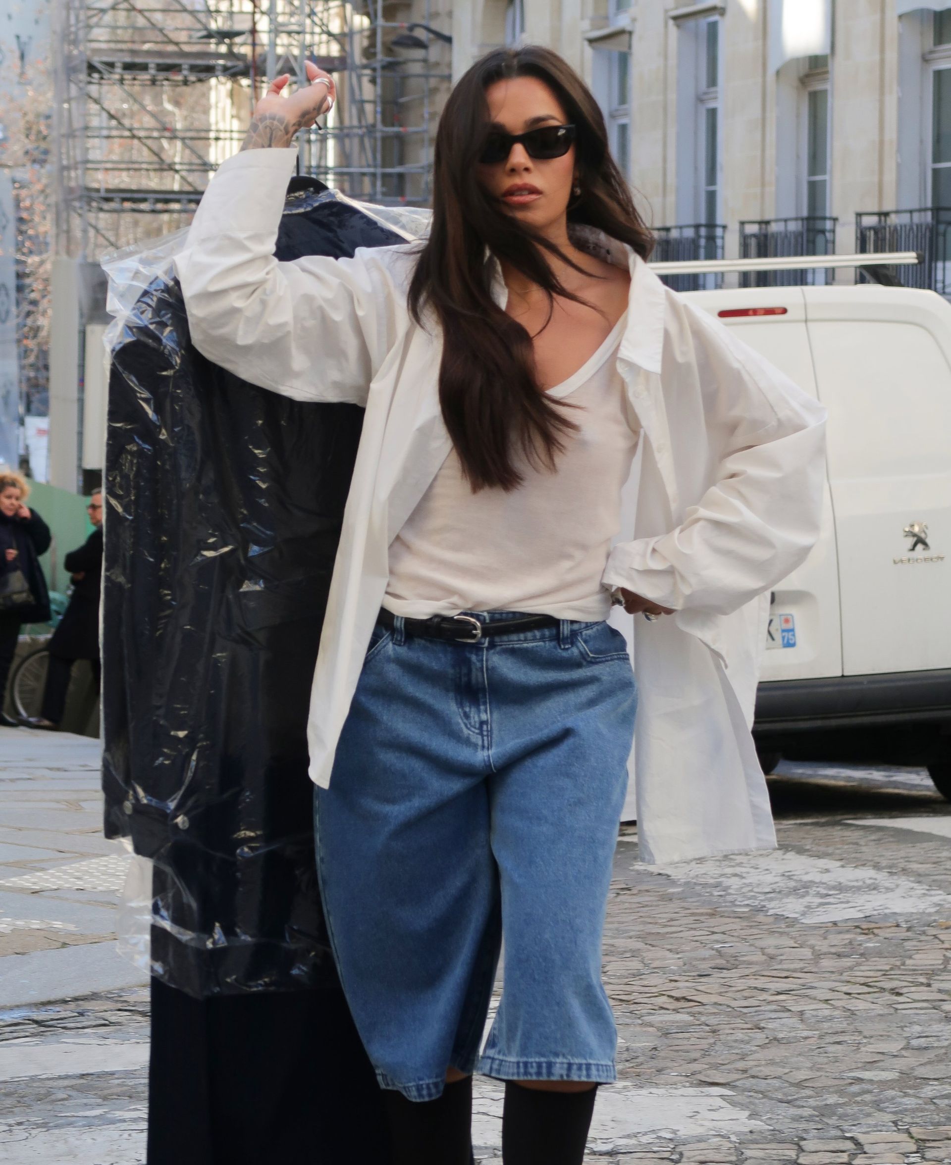 Woman in white oversized shirt and denim skirt holding garment bag on city street