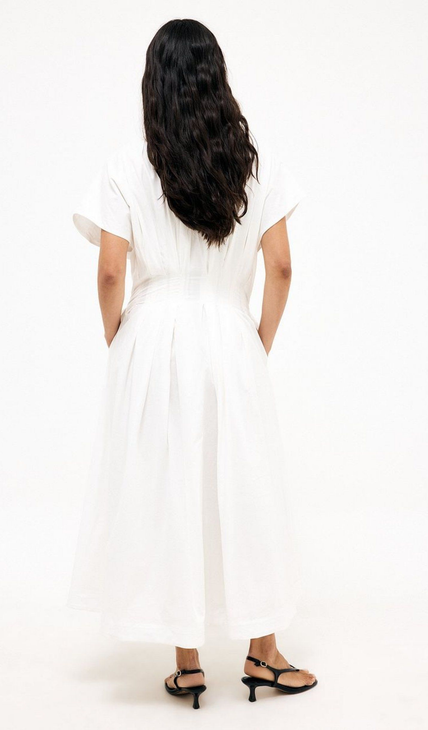 Model shown from the back wearing a white midi dress with short flutter sleeves and a gathered waist in a studio setting